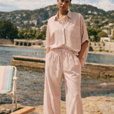 Conjunto riscado branco e rosa com calças largas e camisa de manga curta, ambiente exterior marítimo.