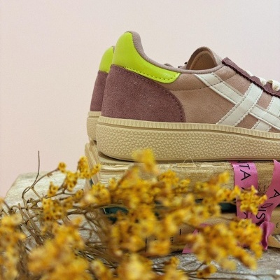 Ténis castanhos com detalhes brancos e verde fluorescente sobre livros com fita rosa, flores amarelas desfocadas