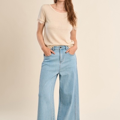 Mulher com t-shirt bege de mangas com renda e calças de ganga largas azuis claras