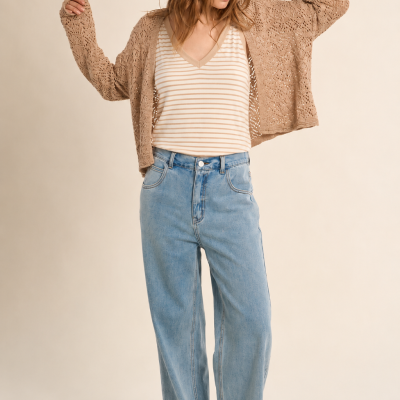 Mulher com camisola às riscas e cardigan bege, jeans largos e sapatilhas brancas num fundo neutro.