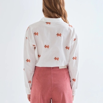 Blusa branca com padrão de cães laranja e calças de veludo cotelê rosa vista de costas.