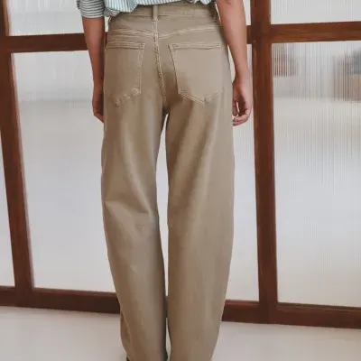 Pessoa de costas com calças largas bege e camisa azul riscada em ambiente interior