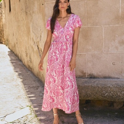 Vestido longo rosa com padrão floral e sandálias douradas numa rua de pedra