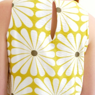Parte de trás de vestido ou top amarelo com flores brancas e abertura com botão
