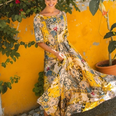 Vestido longo estampado amarelo com flores usado por mulher junto a parede amarela