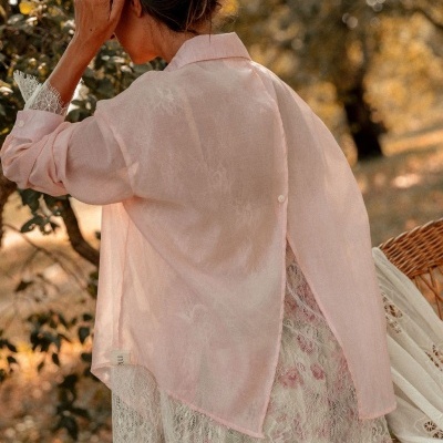Blusa rosa clara semi-transparente com renda e botão, vista de costas, ambiente natural