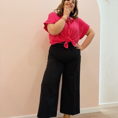 Mulher com camisa rosa e calças pretas em ambiente interior