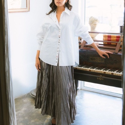 Mulher com camisa branca e saia cinza plissada ao lado de piano antigo