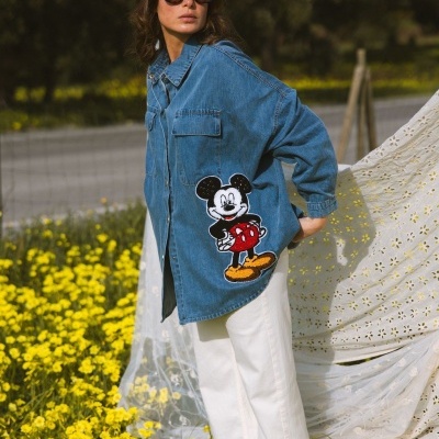 Mulher de camisa de ganga azul com Mickey Mouse junto a flores amarelas