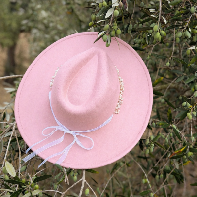 Chapéu rosa de feltro com fita branca e pérolas pendurado em ramo com folhas e azeitonas verdes
