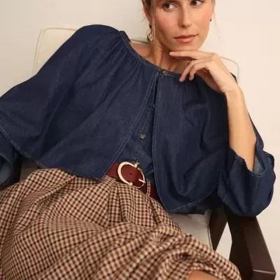 Mulher sentada com capa azul escura e saia plissada aos quadrados castanhos