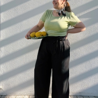 Mulher com roupa casual verde e preta segurando prato com limões, em parede branca e piso de calçada