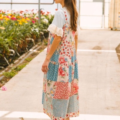 Mulher de perfil com vestido patchwork colorido e camisa branca com renda, em estufa de flores.