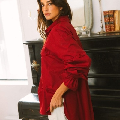 Mulher com camisa vermelha e calças claras em frente a um piano preto