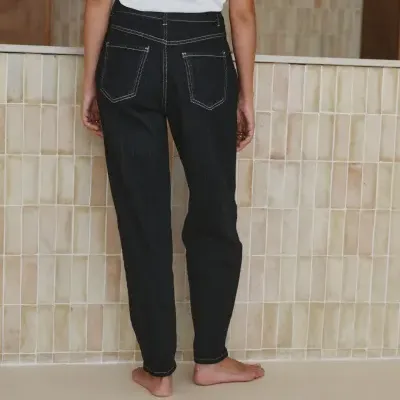 Pessoa de costas vestindo calças de ganga pretas e t-shirt branca com fundo de azulejos beje