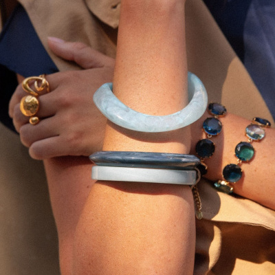 Pulseiras com diferentes cores e materiais e anel dourado no braço e mão de mulher com roupa bege