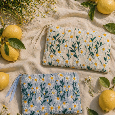Duas bolsas bordadas com padrão de margaridas ao lado de limões e flores sobre tecido claro
