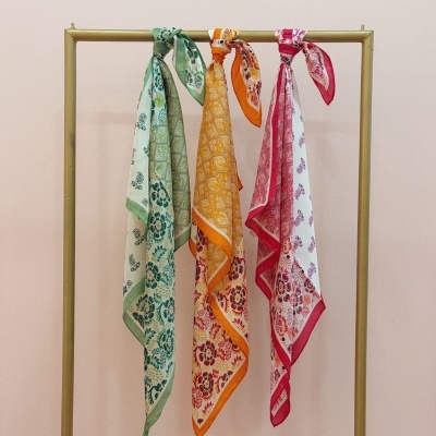 Três lenços coloridos com padrões florais pendurados numa estrutura metálica dourada.