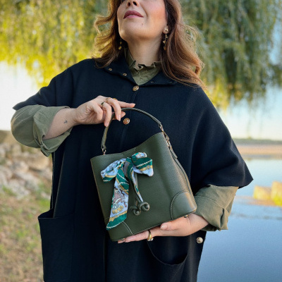 Mulher com capa preta e mala verde com laço colorido