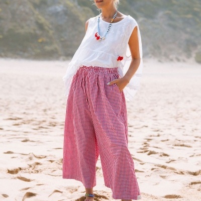 Mulher com calças xadrez vermelhas e brancas, camisa branca, óculos de sol e sapatilhas rosa na praia