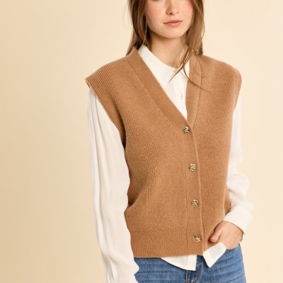 Mulher com colete castanho de malha com botões dourados, camisa branca e calças de ganga azuis