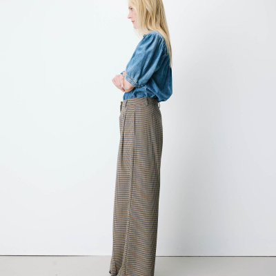 Pessoa de perfil com blusa denim azul e calças xadrez castanhas