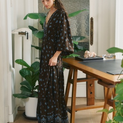 Mulher a usar vestido comprido castanho com flores azuis e botas pretas em ambiente interior