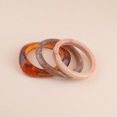 Três pulseiras redondas em tons castanho, bege e âmbar com textura marmoreada