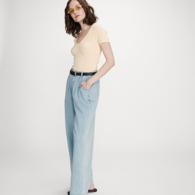 Mulher com camisola bege, calças de ganga largas azul claro, cinto preto, sapatos pretos e óculos amarelos