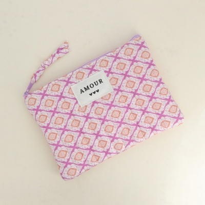 Necessaire em tecido com padrão geométrico lilás, branco e bege com etiqueta AMOUR