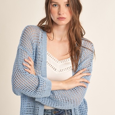 Mulher com camisola azul de malha aberta, camisa branca e jeans de ganga azuis