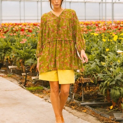 Mulher com blusa floral verde e calções amarelos numa estufa florida