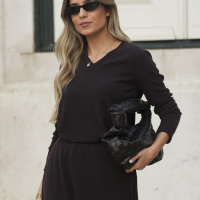 Mulher com vestido preto, óculos de sol pretos e mala preta trançada.
