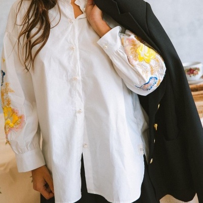 Camisa branca com bordados coloridos nas mangas e casaco preto com botões dourados
