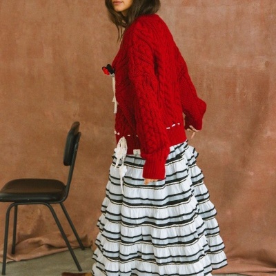 mulher com casaco de malha vermelho e saia branca com riscas pretas