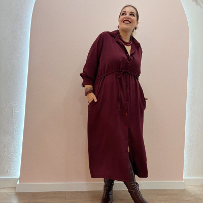 Mulher de vestido midi vinho com botas castanhas num ambiente com parede clara