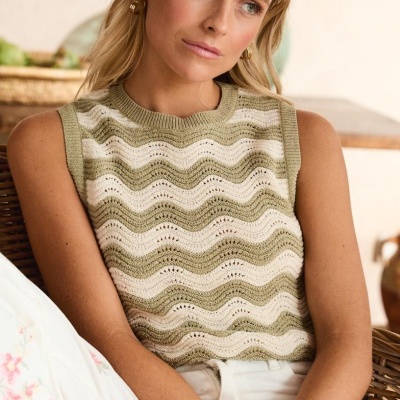 Top de malha verde e creme com padrão de ondas, usado por mulher sentada
