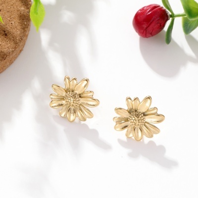 Brincos dourados em forma de flor em fundo branco com decoração de folhas e flor vermelha