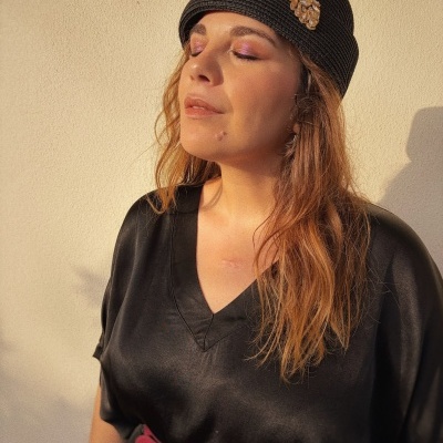 Mulher com chapéu preto de tecido trançado com aplique dourado, vestido preto e cinto vermelho