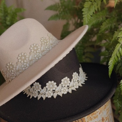 Dois chapéus tipo fedora branco e preto com faixa floral colocados sobre objeto enferrujado