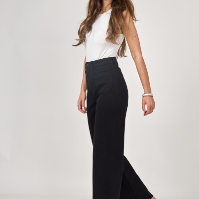 Modelo feminina com calças pretas largas e blusa branca, sapatos brancos com salto e acessórios prateados.