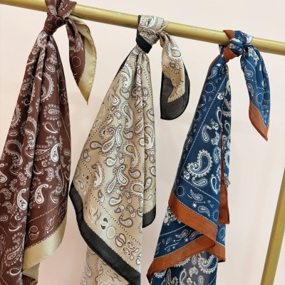 Três lenços de seda com padrão paisley pendurados num suporte dourado.