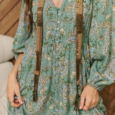 Vestido feminino verde com padrão floral e arabesco, botões frontais e mangas compridas.