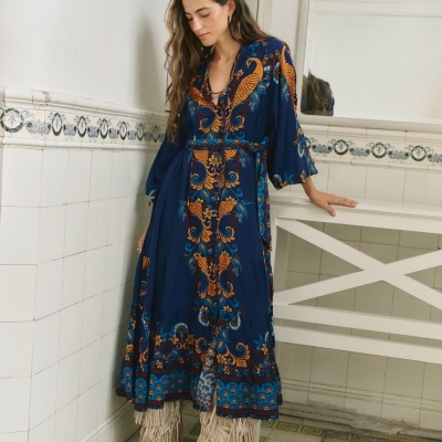 Vestido azul comprido com padrão floral e botas bege com franjas em interior com azulejos