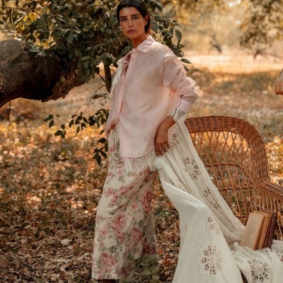 Mulher com camisa rosa e saia floral em ambiente ao ar livre com cadeira de vime.