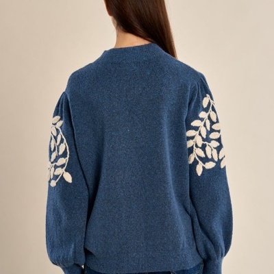 Camisola azul de malha com bordados brancos nas mangas vista de costas