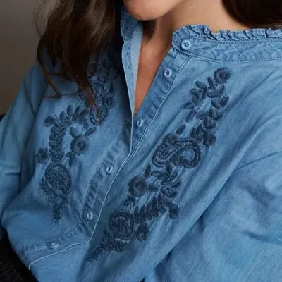 Camisa azul claro com bordados florais azuis escuros e botões frontais