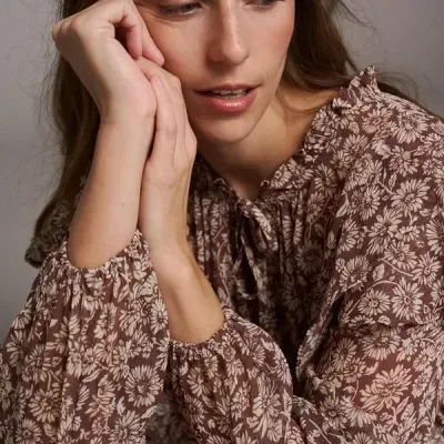 Blusa floral bege e castanha com mangas compridas e laço no decote usada por mulher
