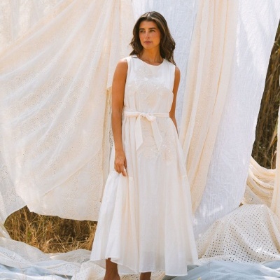 Vestido comprido branco com cinto e bordados em ambiente exterior com tecidos rendados ao fundo