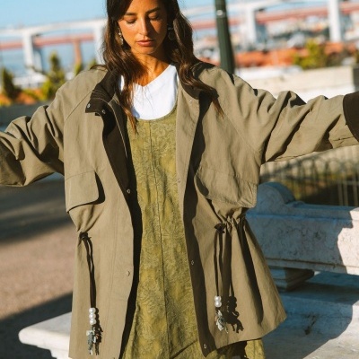 Mulher com casaco bege oversize e vestido verde com padrão floral em ambiente urbano ao ar livre